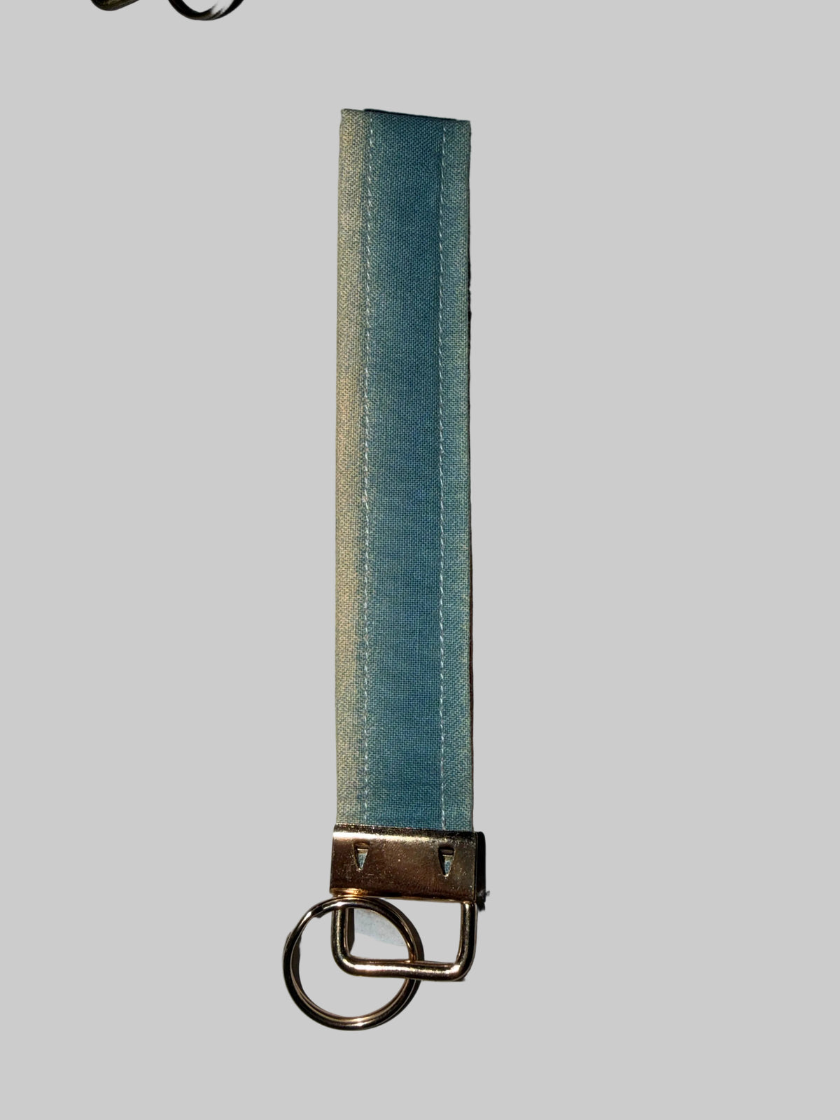 A light blue fabric strap with a brass metal clasp and a split key ring, shown vertically on a light gray marble-like surface.