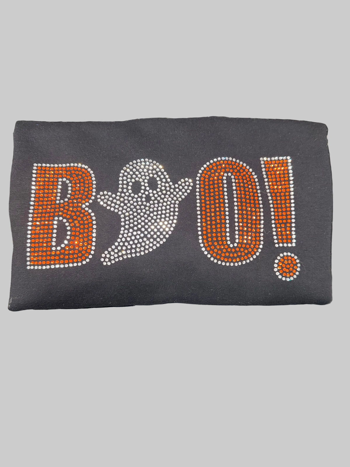 A black sweatshirt covered in rhinestones spelling 'BOO!' with a ghost graphic, placed on a dark marble countertop.