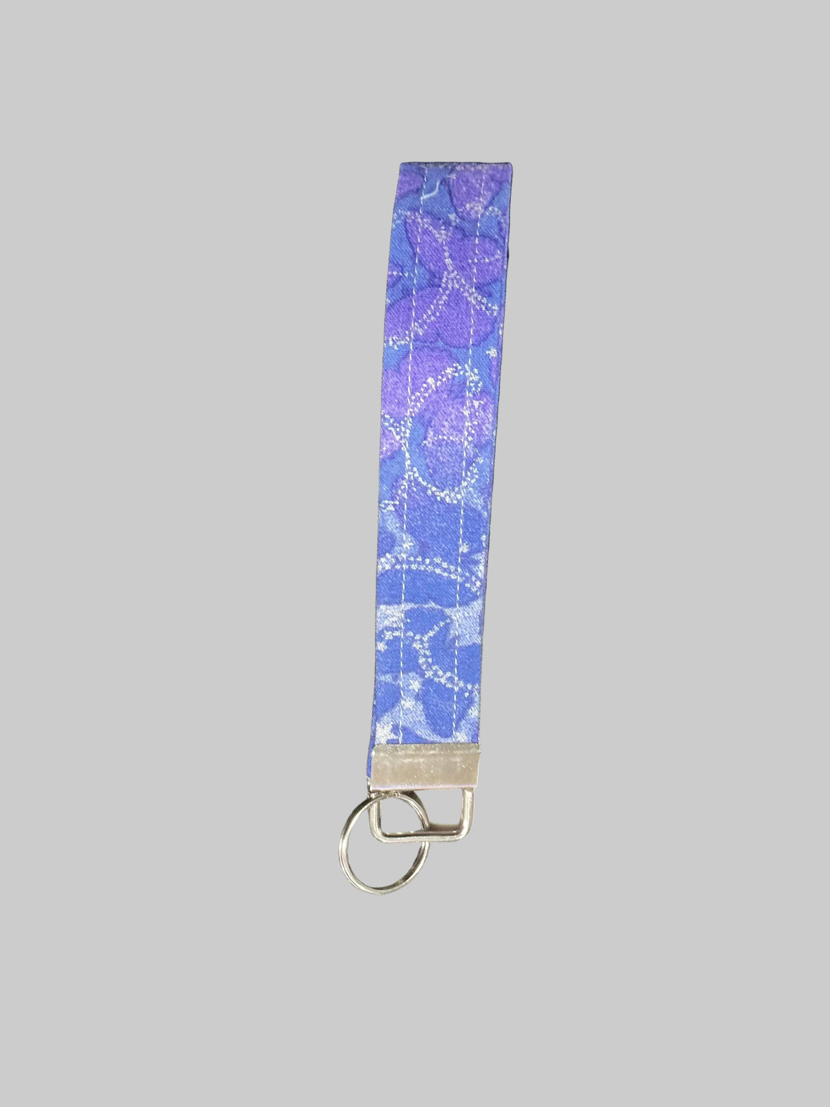 A fabric wristlet strap keychain featuring a blue and purple butterfly pattern with white dotted details, finished with a silver metal split ring and clasp, set against a solid gray background.