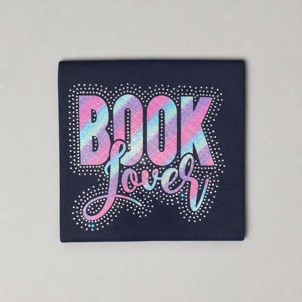 A square dark navy graphic print featuring the word 'BOOK' in large glittery pink and iridescent letters with decorative swirls and white dotted outlines, shown on a light gray background.