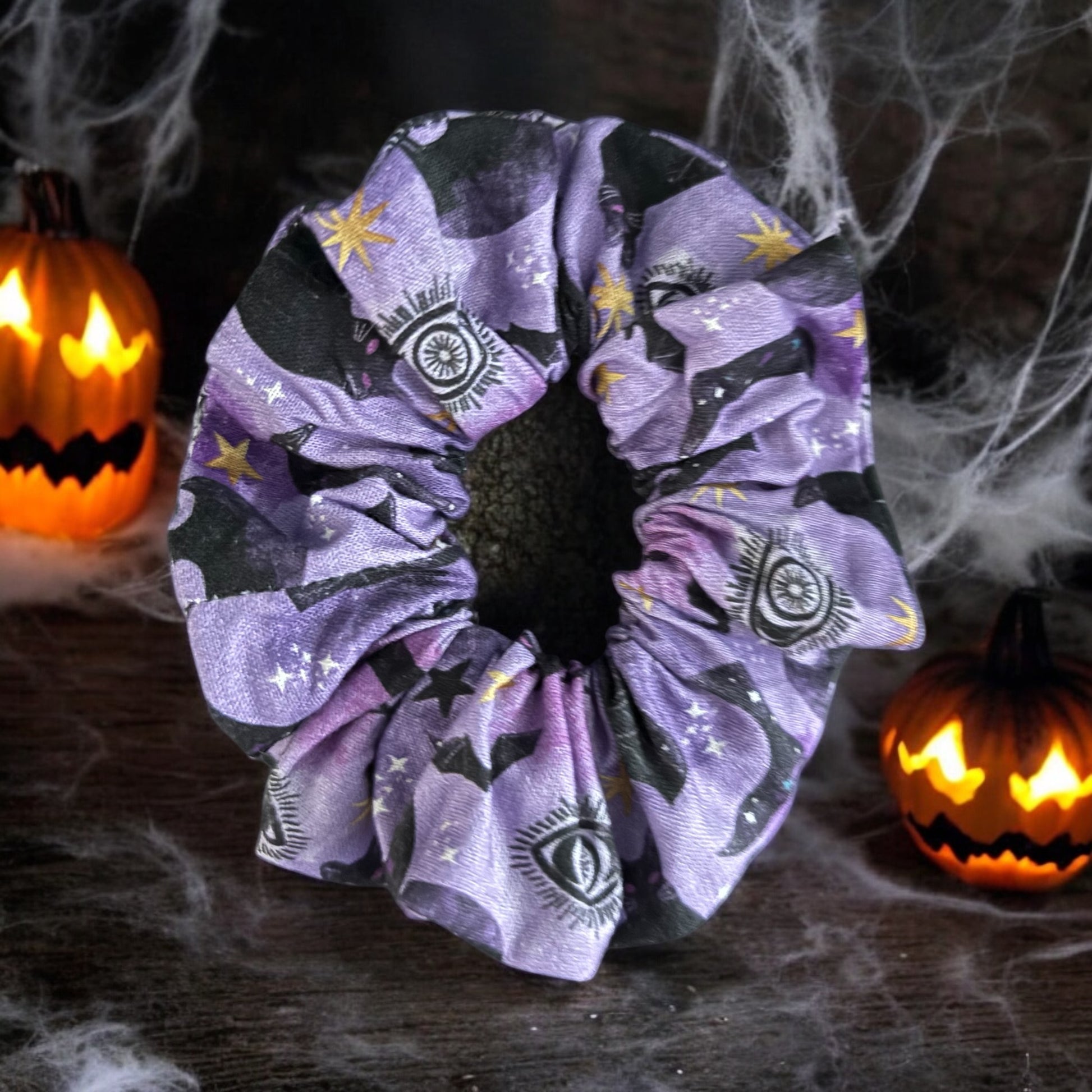 Halloween-themed scrunchie with Cats and all seeing eye with Pumpkins and spider webs in the background