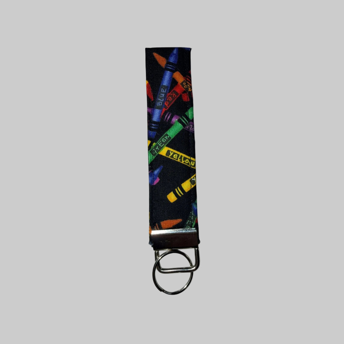 A fabric keychain strap featuring a colorful crayon print on a black background, finished with a silver metal clasp and split ring, shown against a plain white background.