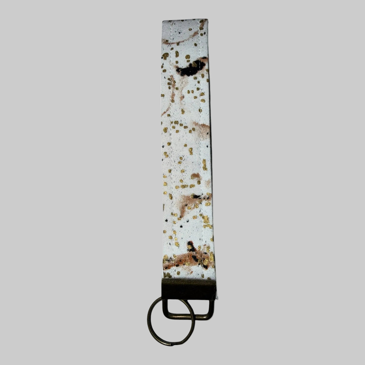 A long, narrow white strap or belt with a distressed, speckled pattern of gold, brown, and black, finished with a dark metal ring at the bottom.