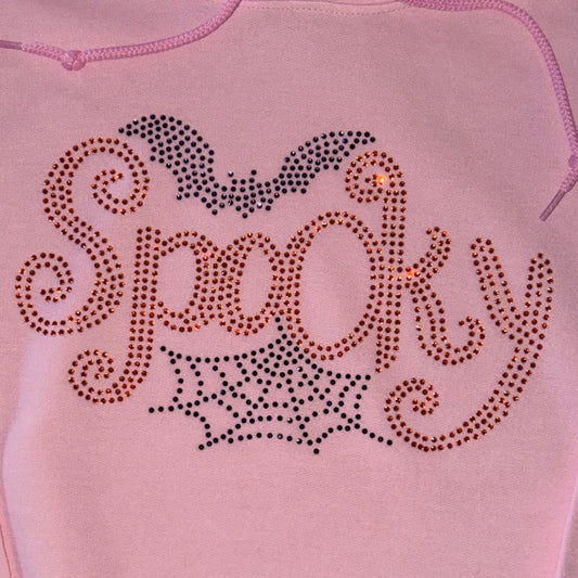 A light pink hoodie featuring a rhinestone-studded 'Spooky' graphic on the chest, complete with a bat and spiderweb design.