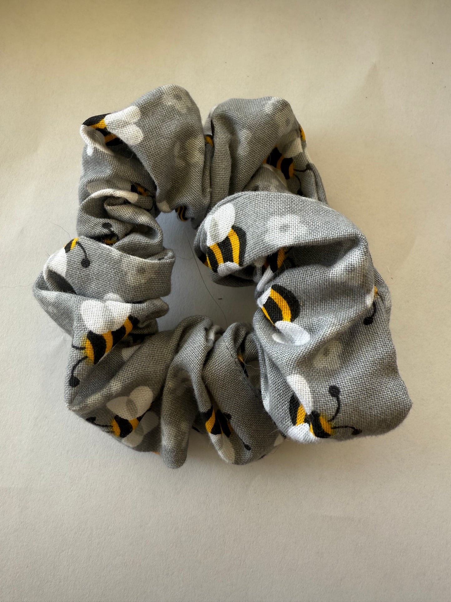 Gray scrunchie with bee pattern on a beige background