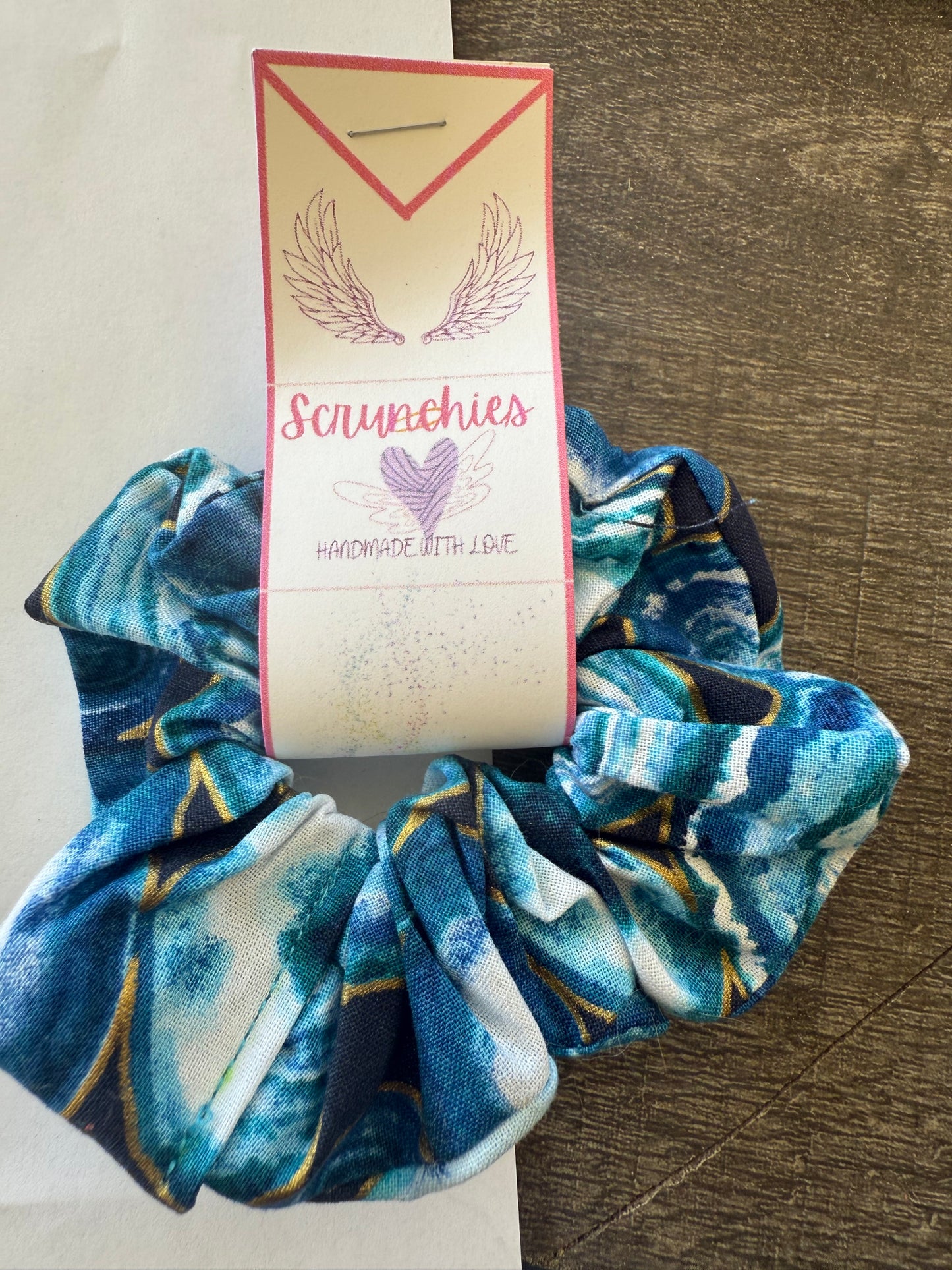 Blue and white patterned scrunchie with a branded tag on a neutral background