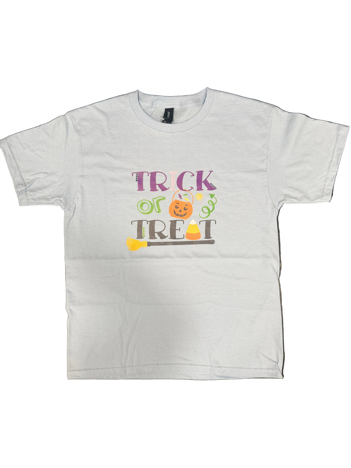 A light blue short-sleeve t-shirt with a colorful 'TRICK or TREAT' Halloween graphic, laid flat on a dark marble countertop.