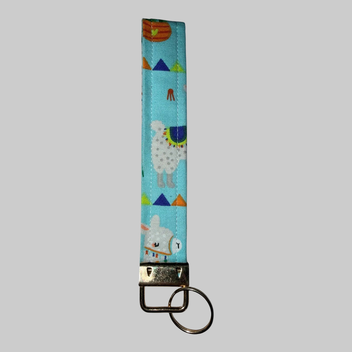 A fabric keychain strap with a light blue background and a whimsical alpaca and llama pattern, finished with a silver metal clasp and keyring.