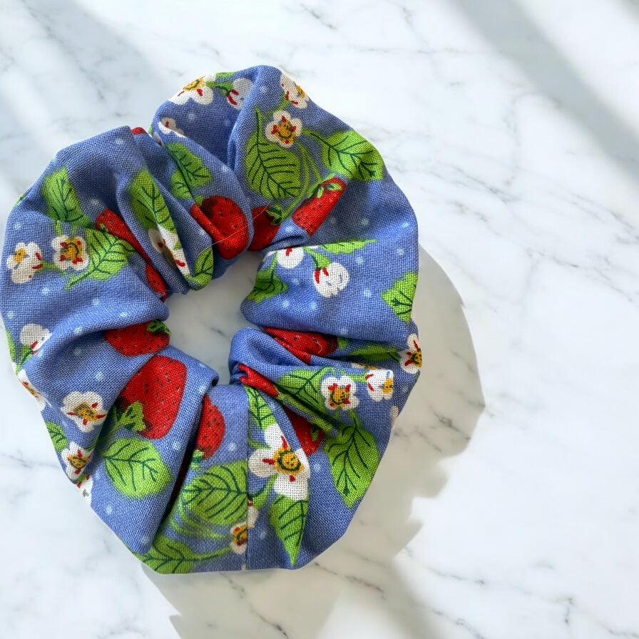 Blue scrunchie with strawberries and floral and leaf pattern on a marble surface