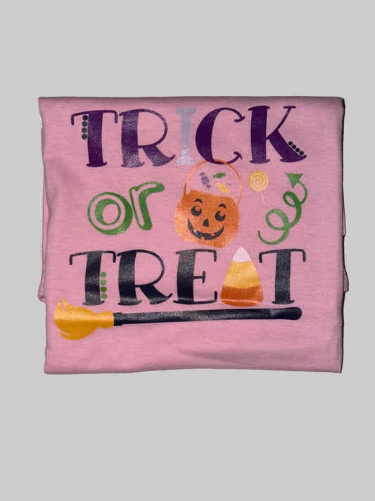 A folded pink t-shirt with a 'Trick or Treat' Halloween graphic, laid flat on a light beige tiled floor.