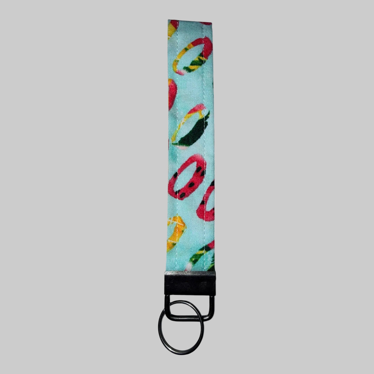 A fabric keychain strap with a light blue background and a colorful pattern of red, yellow, and green abstract shapes, finished with a black metal split ring.