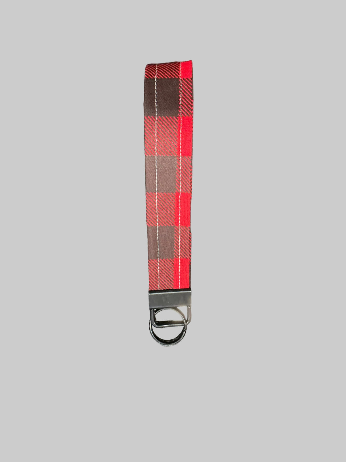 A red and black plaid fabric wristlet strap with a silver metal clasp and key ring, shown against a solid gray background.
