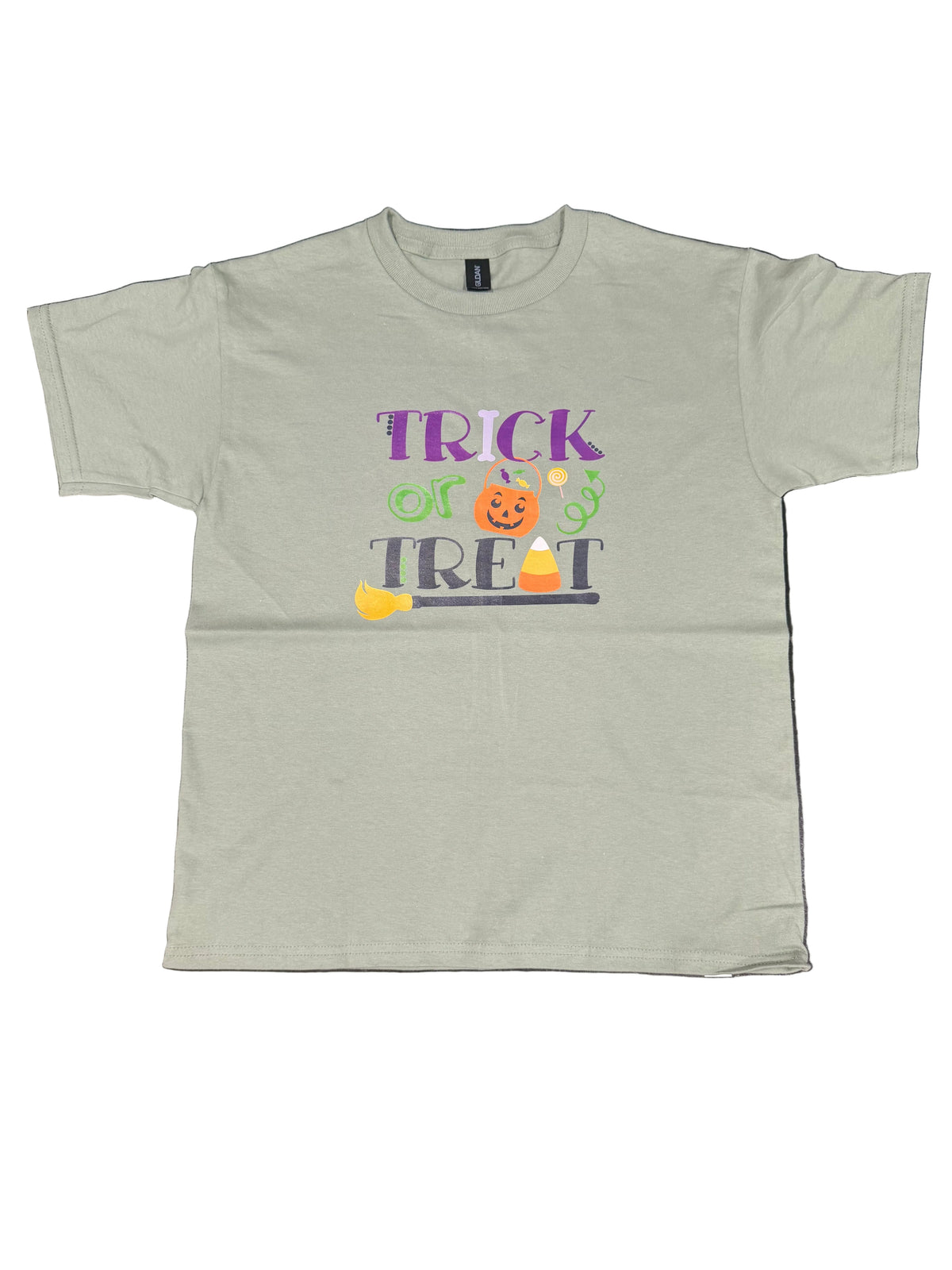 A light sage green short-sleeve t-shirt with a 'Trick or Treat' Halloween graphic, laid flat on a black marble surface.