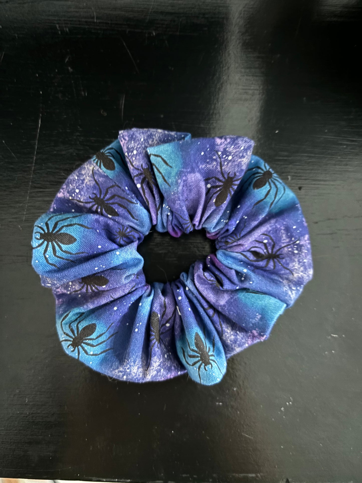 Blue scrunchie with spider design on a dark surface